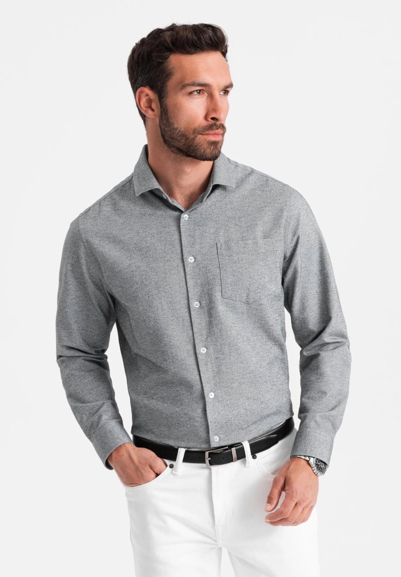 Chemise grise à boutons avec un motif texturé, dotée d'une poche poitrine, associée à un pantalon blanc et une ceinture noire, présentée sur un fond uni.