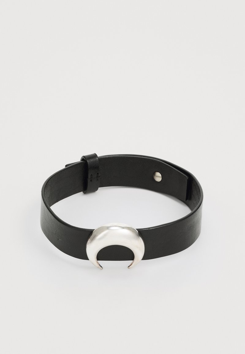 Svart läderarmband med en silverfärgad halvmåneformad metalldetalj, säkrad med en tryckknapp, slät yta och en minimalistisk design.