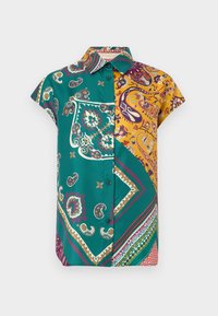 Chemise à manches courtes avec boutons, présentant un patchwork de motifs paisley et géométriques verts et jaunes sur fond blanc.