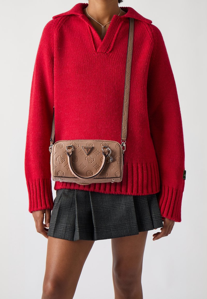 Personne portant un pull en maille rouge et une jupe plissée à carreaux foncés, portant un sac bandoulière beige embossé avec des ferrures argentées.