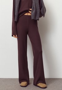 Donkerbruin geribd gebreid tweedelig outfit met lange mouwen en broek met wijde pijpen, gecombineerd met beige instapschoenen. Zachte textuur met een aangesloten pasvorm.