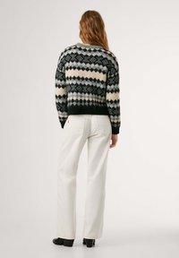 Gebreide trui met een geometrisch patroon in zwart, grijs en beige. Gecombineerd met witte broek en zwarte hakken. Zachte, gestructureerde afwerking.