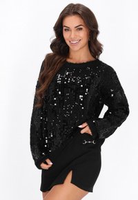 Czarny dzianinowy sweter z cekinami, o luźnym kroju, z teksturowanymi rękawami i okrągłym dekoltem, w połączeniu z czarną spódnicą z bocznym rozcięciem i metalowymi detalami.