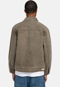 Olijfgroene denimjack met een klassiek kraag en knoopsluitingen op de mouwen, met een rechte snit en zichtbare stiksels aan de achterkant.
