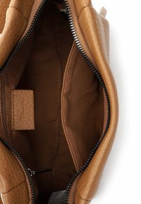 Brązowe wnętrze teksturowanej skórzanej torebki z zamknięciem na zamek błyskawiczny, z podszewką materiałową, jedną otwartą kieszenią i oznakowaną przegrodą.