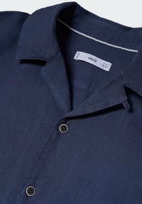 Granatowa lniana koszula z kołnierzykiem typu włoskiego, dwoma czarnymi guzikami oraz metką wewnątrz. Charakteryzuje się miękką fakturą i swobodnym designem.