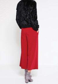 Svart fuskpälsjacka, röda vida byxor och grå ankelstövlar. Byxorna har sidofickor och en slät, flödande tyg.