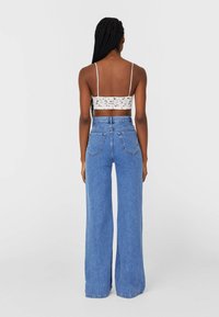 Witte kanten cropped top met dunne bandjes, gecombineerd met een high-waisted, wijde blauwe spijkerbroek met achterzakken en een vervaagde textuur.