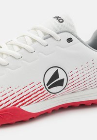 White athletic shoe with red and black accents, featuring a mesh upper, laces, and textured rubber sole with a dynamic stripe pattern.