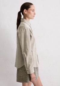 Beige katoenen overhemd met knoopsluiting, losse pasvorm en lange mouwen, gecombineerd met een gestructureerde geruite rok in aardetinten.