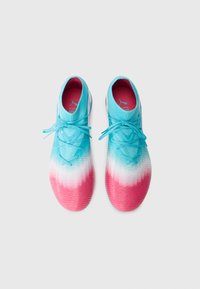Une paire de chaussures de football dégradées en bleu, blanc et rose avec des lacets sur un fond blanc, vue de dessus.