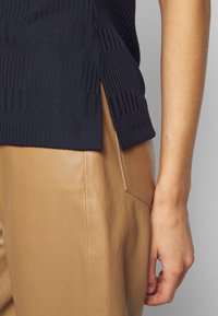 Granatowy sweter z dzianiny z teksturowanymi paskami oraz bocznymi rozcięciami. Połączony z jasnobrunatnymi skórzanymi spodniami z tylną kieszonką. Gładki, dopasowany krój.