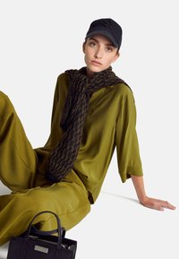 Cappello da baseball nero, sciarpa a fantasia marrone scuro e nera, top verde oliva, pantaloni abbinati e una piccola borsa nera con manici.