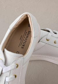 Baskets en cuir blanc avec une finition texturée, lacets plats et œillets dorés. Dotées d'un intérieur rembourré et d'un design minimaliste.