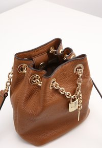 Sac seau en cuir marron avec une surface texturée, quincaillerie dorée, accent en chaîne et ouverture à cordon de serrage. Comprend une sangle amovible.