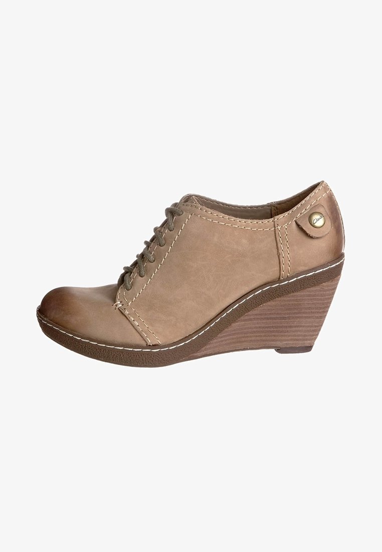 Bordowe buty na koturnie z jasnobrązowej skóry z zapięciem na sznurówki, okrągłym noskiem, białym przeszyciem i fakturowaną brązową podeszwą. Posiadają złoty guzik jako akcent.