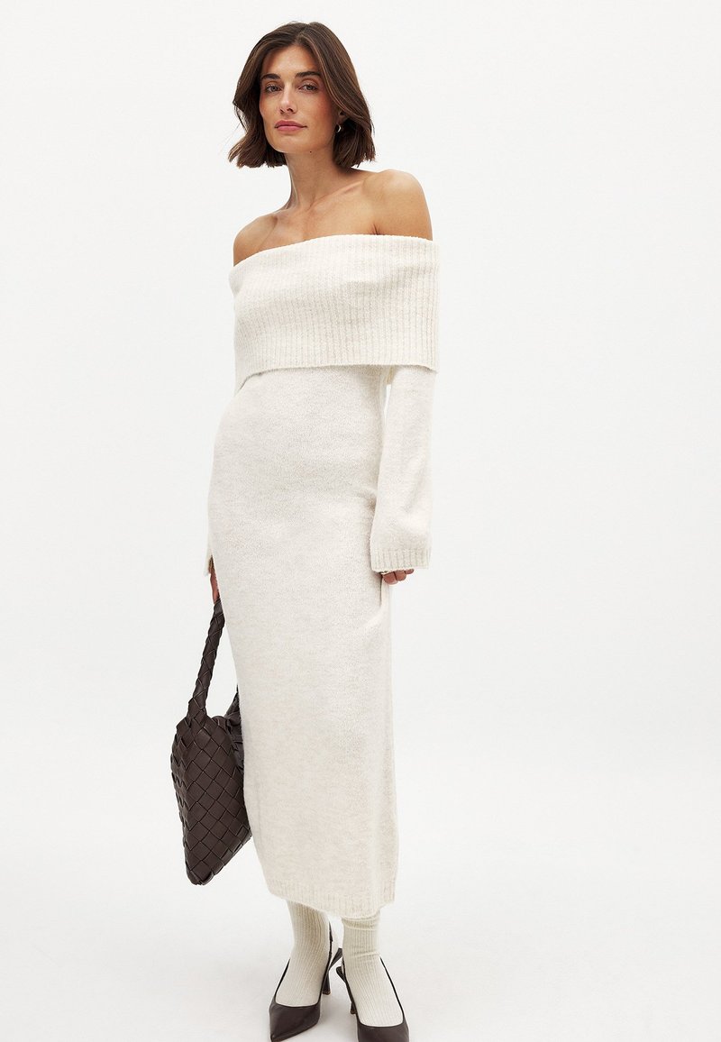 Õla pealt avatud, pika varrukaga koorevalge kleit, mis on valmistatud pehmest kudumifaas, sobiva silueti ja soonikuaktsentidega kaeluses ja mansettides.