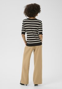 Top en tricot à rayures noir et blanc avec des manches courtes, associé à un pantalon tan ample et des talons noirs. Design simple, texture douce.