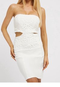 Valkoinen kahdesta osasta koostuva mekko, jossa on olkaimeton lyhyt yläosa kukkakuvioisesta pitsistä ja tiukka hame, jossa on aukkoja, esittelee tekstuurisia materiaaleja.