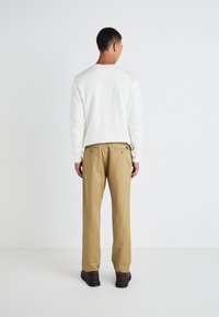 Crewneck sweatshirt in white, paired with khaki straight-leg trousers featuring back pockets; model wearing dark brown shoes.