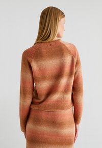 Sweatshirt en tricot dans des dégradés de rouille et de crème, avec un col rond et des manches raglan ; texture douce avec des transitions de couleur subtiles.