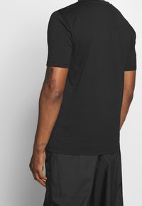 Mustat lyhythihaiset t-paidat, joissa on pyöreä kaula-aukko, pehmeä kangas ja yksinkertainen muotoilu. Sisältää ompeluyksityiskohtia hihoissa ja helmoissa.