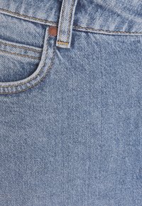 Světle modré džíny z denimu s typickým pětikapsovým designem, viditelným prošíváním a měděným knoflíkem na pásku.