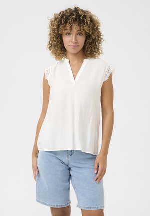 Top bianco a maniche corte con scollatura a V e dettagli in pizzo sulle spalle, abbinato a pantaloni corti di jeans blu chiaro. Tessuto morbido, vestibilità casual.