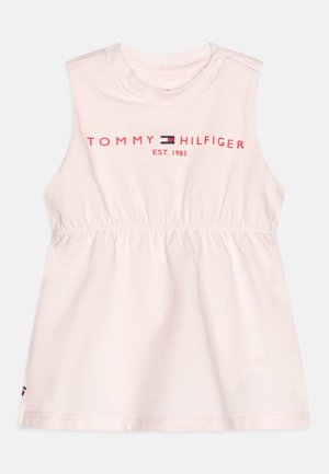 Lichtroze mouwloze jurk met een geplooide taille, met de tekst "TOMMY HILFIGER EST. 1985" in het rood boven een logo. Zachte katoenen stof.