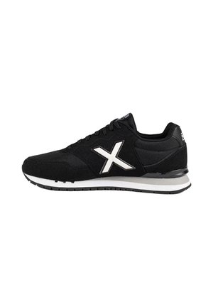 Zapatilla negra con suela blanca y gran logo blanco en forma de X en el lateral, cierre con cordones y cuello acolchado, visible desde la vista lateral izquierda.