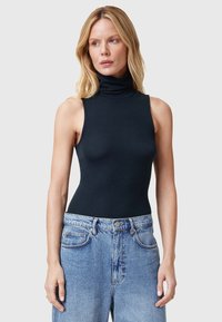 Top negro de canalé sin mangas con cuello perkins, combinado con jeans de mezclilla ligera de corte alto. Textura suave, diseño ajustado.