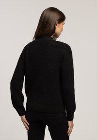 Czarny sweter dzianinowy z prążkowanym wykończeniem u dołu i na rękawach, z okrągłym dekoltem i teksturowanym wzorem. Widok od tyłu.