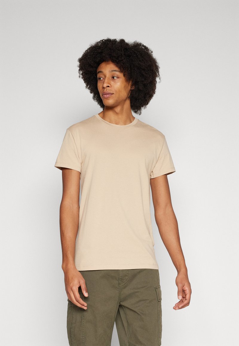Beige T-shirt met ronde hals in een zachte, gladde stof. Korte mouwen en een standaard pasvorm. Gedragen met olijfgroene cargoshorts met zakken.