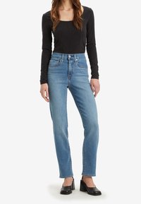 Blå högmidjade jeans med rak silhuett, med silverfärgade nitar på framfickorna, i kombination med en svart långärmad topp.