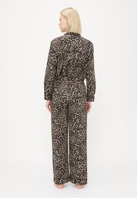 Lepardmønstret pysjamassett i beige og brunt. Skjorten har krage og knapper, mens buksene har vide ben med elastisk midje.