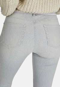 Pantalones de mezclilla a rayas grises y blancos con un diseño ajustado, que cuentan con dos bolsillos traseros y un acabado texturizado sutil.