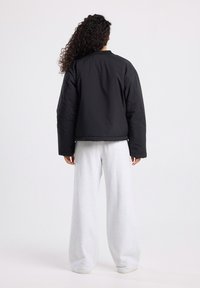 Zwarte cropped pufferjack met een ronde hals, gewatteerde textuur en elastische manchet, gecombineerd met witte, loszittende trainingsbroek.