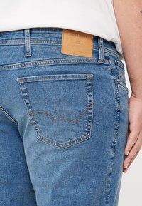 Heledad teksased kerge sinise värviga, millel on nahast silt "JACK & JONES" logoga, tavalised taskud, millel on tagatelgedel kumerad õmblusdetailid.