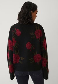 Zwarte gebreide trui met grote rode bloemenpatronen en groene bladeren, met een zachte textuur en een relaxed fit.