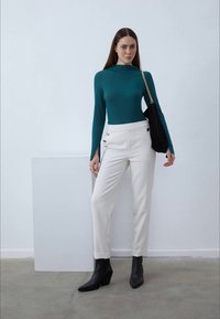 Türkis sinise pikkade varrukatega blouse, valged kohandatud püksid dekoratiivsete nööpidega ja mustad terava ninaga pahkluudepukid. Lihtne must käekott kettrihmaga.
