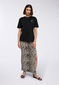 Maglietta nera a maniche corte con un piccolo logo, abbinata a una gonna maxi con stampa leopardata e uno spacco laterale, e sandali neri flat.