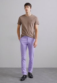 Camiseta castanha de manga curta, calças justas lilás claras e sapatos pretos. Design simples, textura suave e sem padrões ou detalhes visíveis.