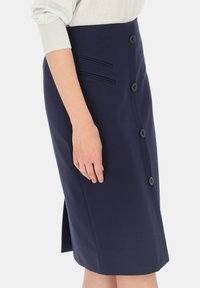 Granatowa spódnica ołówkowa wykonana z gładkiego materiału. Posiada zapięcie na guziki z przodu, fałszywe boczne kieszenie oraz boczny rozporek dla większej swobody ruchów.