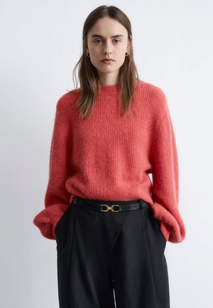Pink wool sweater with a relaxed fit and ribbed texture, paired with black high-waisted trousers and a black belt featuring a gold buckle.
