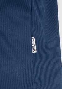 Donkerblauwe ribstof met een gestructureerd oppervlak. Heeft een klein wit label met de tekst "SMILODON" aan de zijkant.