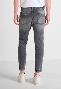 Jeans de denim gris ajustados con un acabado degradado, que presentan bolsillos traseros y detalles de costura mínimos. Llevados con zapatillas blancas.