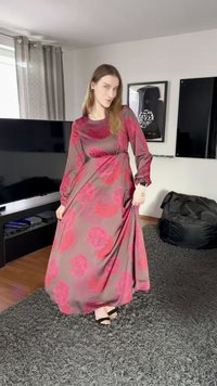 Lang, flytende kjole i mørkebrun med store rosa blomsterprint. Har lange ermer og rund hals, laget av et mykt stoff.