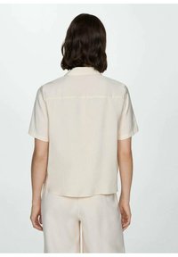 Blusa a maniche corte, color crema, con una vestibilità morbida, dotata di cucitura sul retro e una texture morbida e liscia, progettata per un look casual.