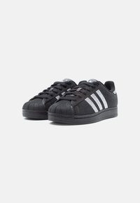 Czarne sneakersy z siateczki, wyposażone w gumowy nosek, teksturowaną cholewkę oraz trzy białe paski po boku. Projekt uzupełniają czarne sznurowadła i podeszwa.