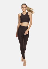 Rjav športni modrček in hlače z visokim pasom iz gladkega, elastičnega materiala. Obe kosi imata minimalne šive in tesno prileganje.